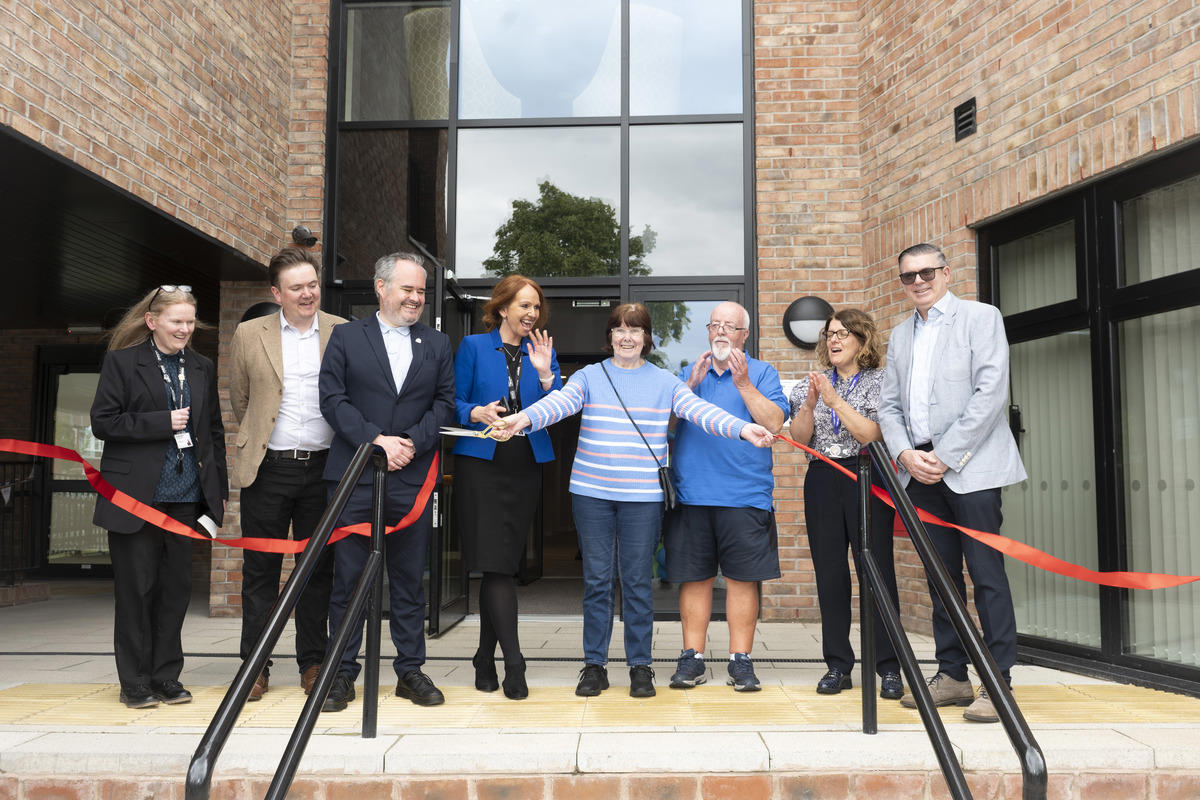 Collection of people in front of building with a red ribbon being cut